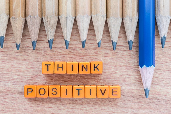 Building blocks spelling out "Think Positive" and one blue pencil standing taller than the rest