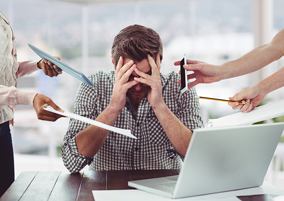 Stressed man at his desk with his head in his hands inundated with distractions at work